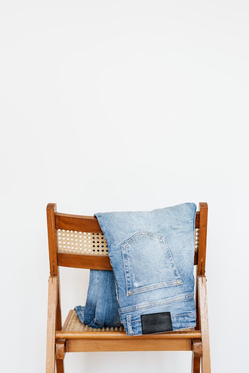 Trendy blue jeans put on back of wooden chair near empty white wall
