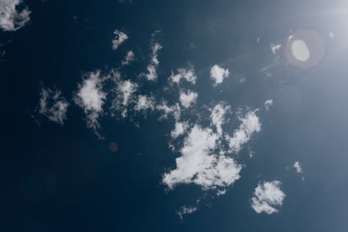 From below of blue sky with clouds and bright sunlight causing lens flare