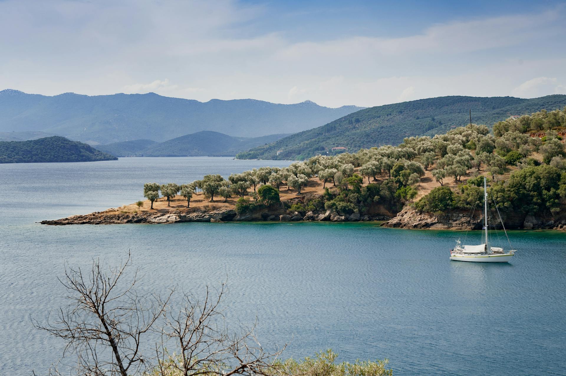 Tranquil bay view in Greece featuring a lone yacht and serene island landscape.