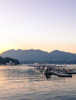 Scenic view of seaplanes docked at Vancouver harbor during sunset with mountains in the background.