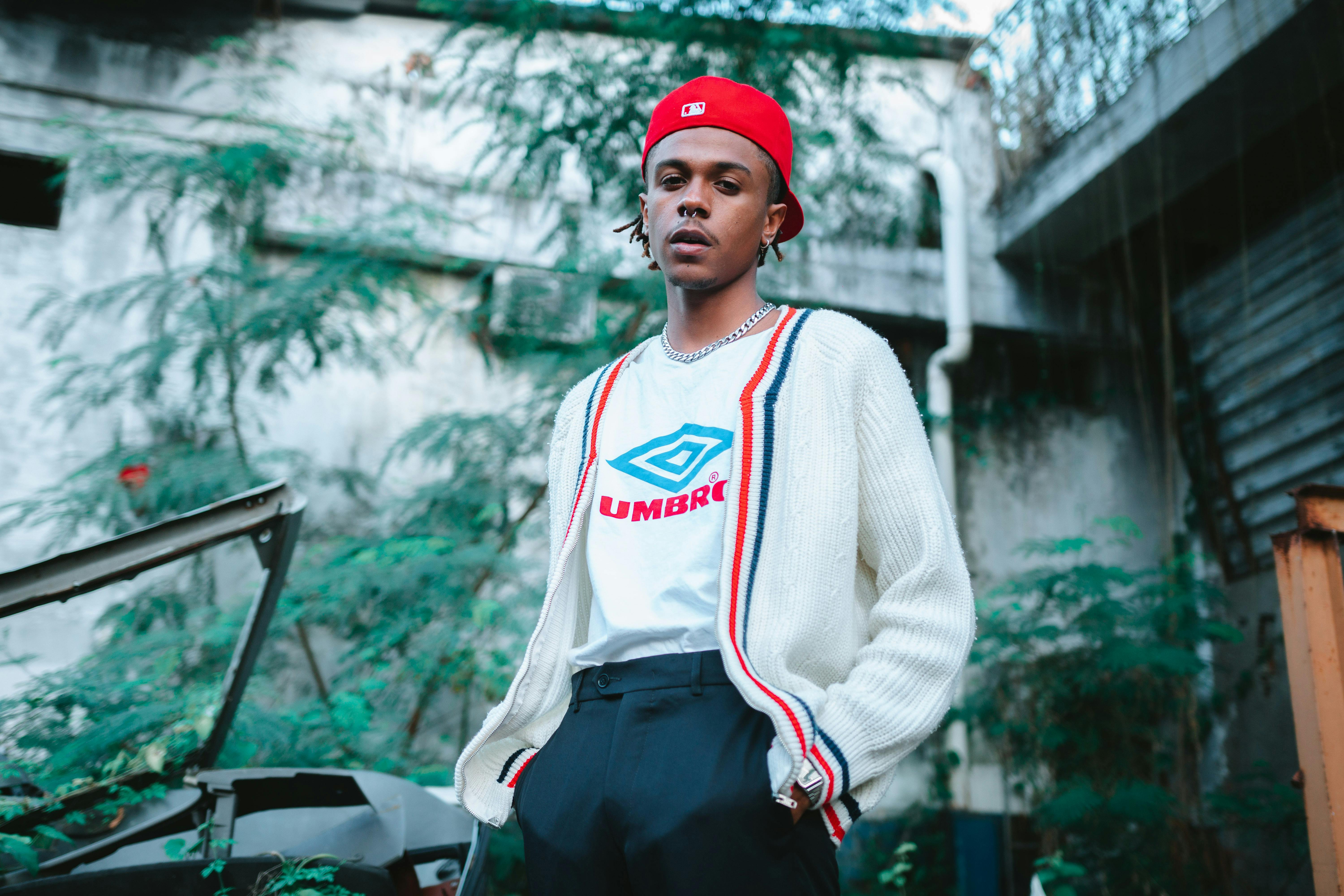 Confident man in white cardigan and red cap in urban setting.