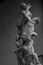 Black and white of aged masonry ornamental statue representing naked male kidnapping woman