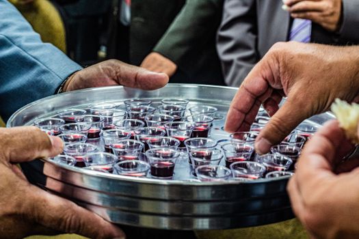 Crop anonymous male with metal tray full of small glasses of red wine for degustation