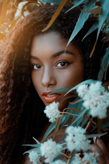 Beautiful portrait of a woman with curly hair surrounded by flowers, showcasing natural elegance.
