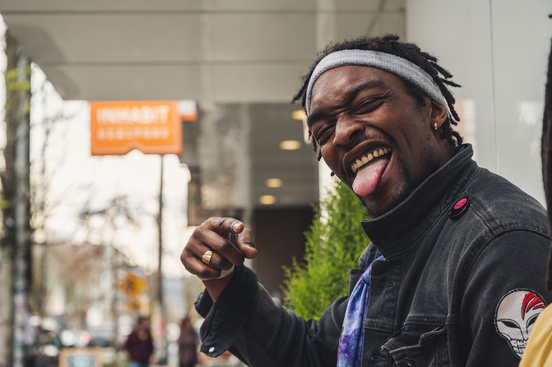 A playful man in a stylish jacket poses outdoors, showing individuality and humor with a funny expression.