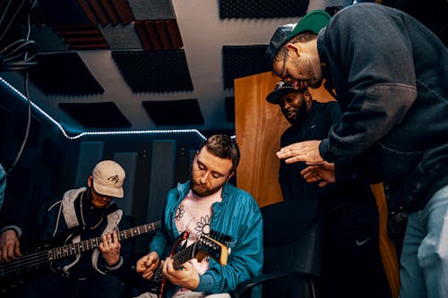 Low angle of artists playing electric guitars near standing multiracial bearded partners in music studio