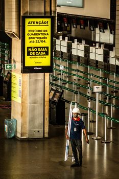 From above of anonymous worker in mask and protective helmet walking with ladder on floor under yellow signboard with information about COVID 19 pandemic