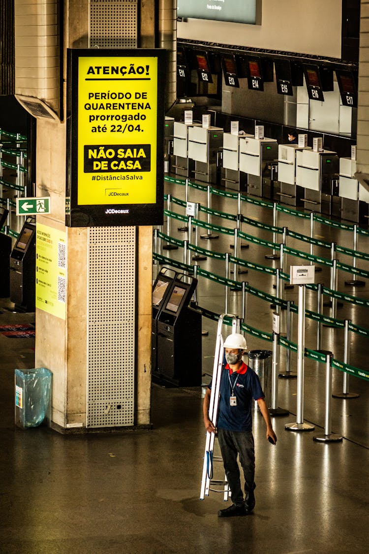 Unrecognizable Workman With Ladder In Airport Under Bright Signboard