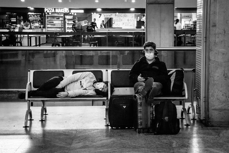 Anonymous Tourists In Masks On Bench In Airport