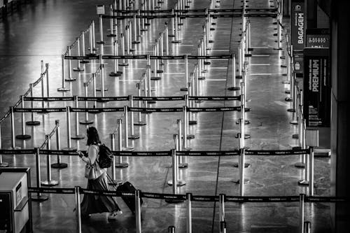 From above black and white side view of unrecognizable female tourist with backpack and suitcase strolling on fenced passage in airport