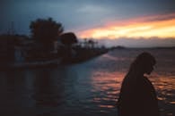 一名女子的剪影映在水边，背景是戏剧性的日落天空