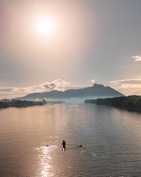 A tranquil lake scene with a lone kayaker under a stunning sunrise and mountain backdrop.