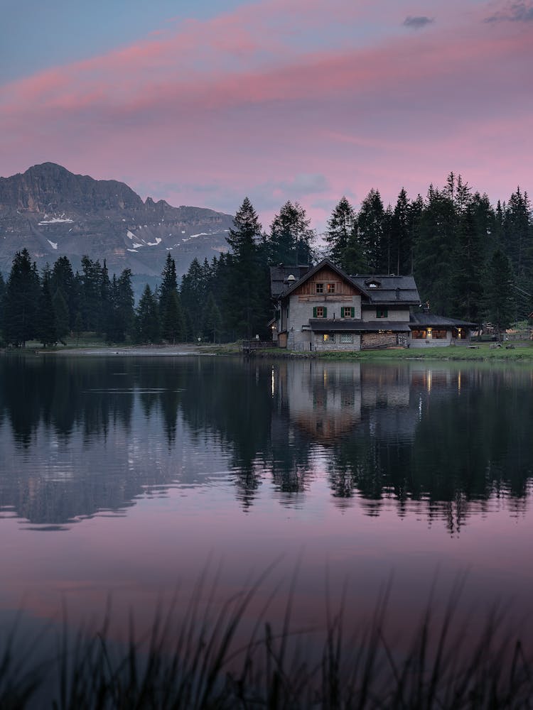 Old House Reflecting In Lake Behind Mountain At Sunset