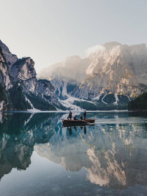 無料 山の近くの湖の茶色のボートの人々 写真素材