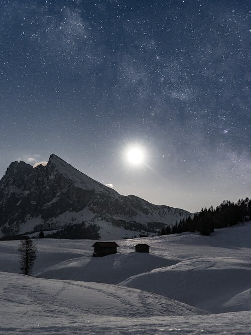 Small houses on snowy hills near mount and shiny sun