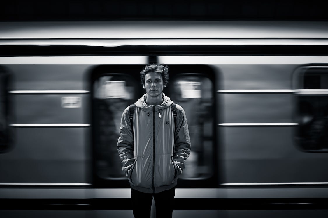 Free Man Wearing Windbreaker Jacket Standing on Train Station Grayscale Photography Stock Photo