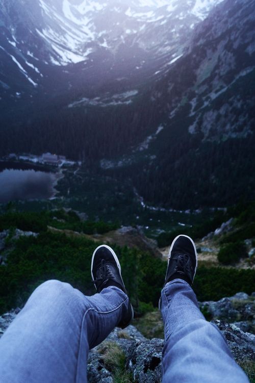 Free View of person sitting atop a mountain ledge, overlooking a scenic landscape. Stock Photo