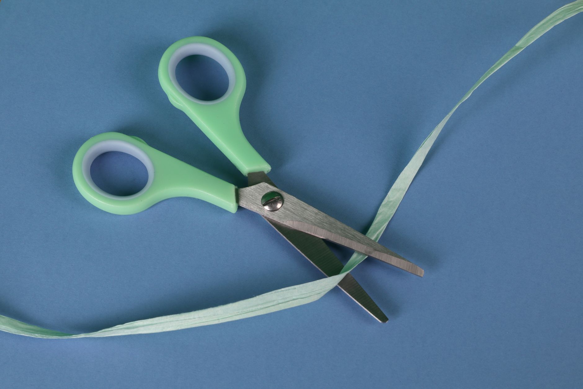 Green handled scissors cutting ribbon on a blue background, showcasing sharp cutting tools.