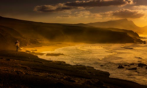 Unrecognizable tourists on mountain near wavy sea at bright sunset