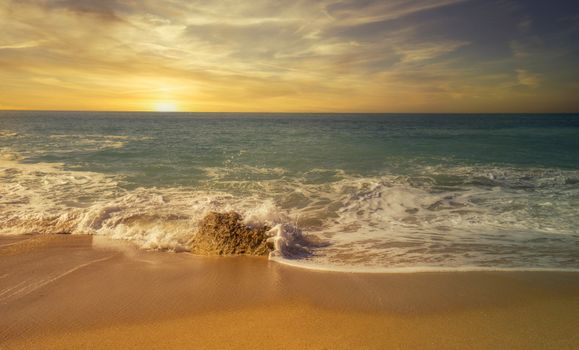 Golden sunset over a calm beach with gentle waves and a vibrant sky.