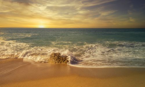 Free Golden sunset over a calm beach with gentle waves and a vibrant sky. Stock Photo
