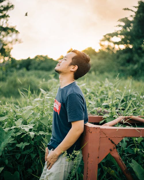 Photo of Man Closing His Eyes While Standing Near Green Plants