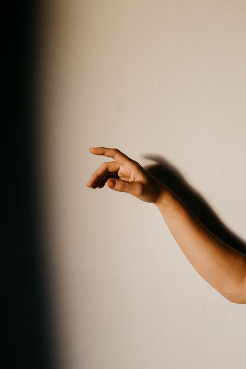 Free A minimalist close-up of a hand making a gesture against a dimly lit wall. Stock Photo
