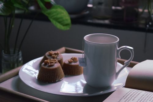 Free Aromatic hot tea in white ceramic cup placed on plate with delicious chocolate cupcakes near opened book in light room Stock Photo