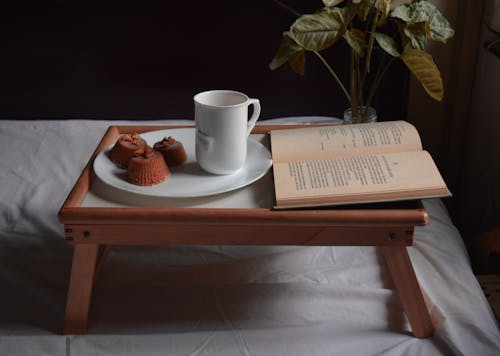 Cup of tea and dessert near book on bed tray