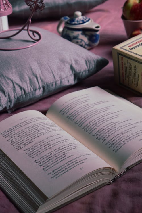 Free High angle arrangement of interesting opened book on soft bed placed near ceramic milk jar and pillows Stock Photo