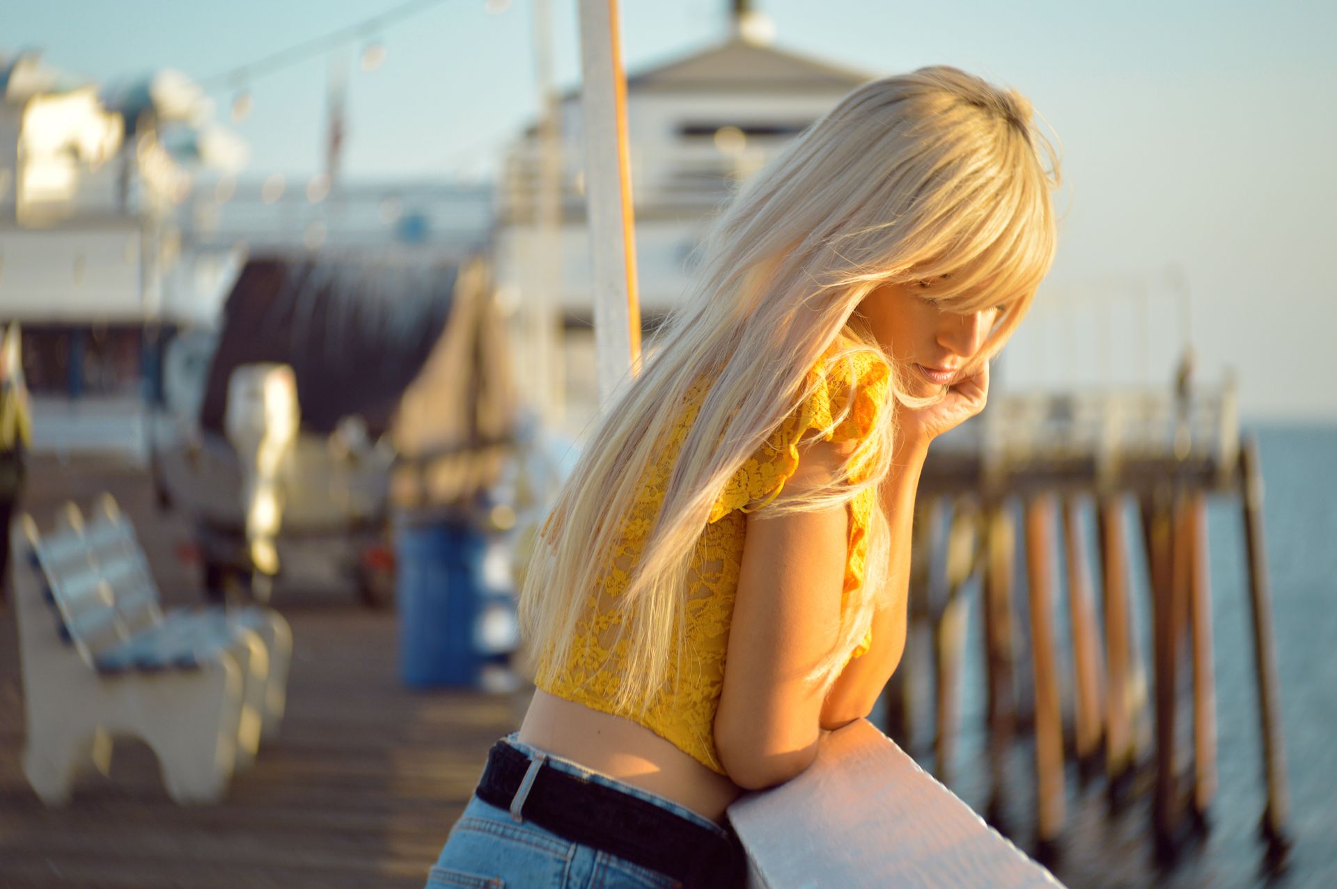 A blonde woman with long hair leans on a railing at Malibu Pier during sunset, deep in thought.