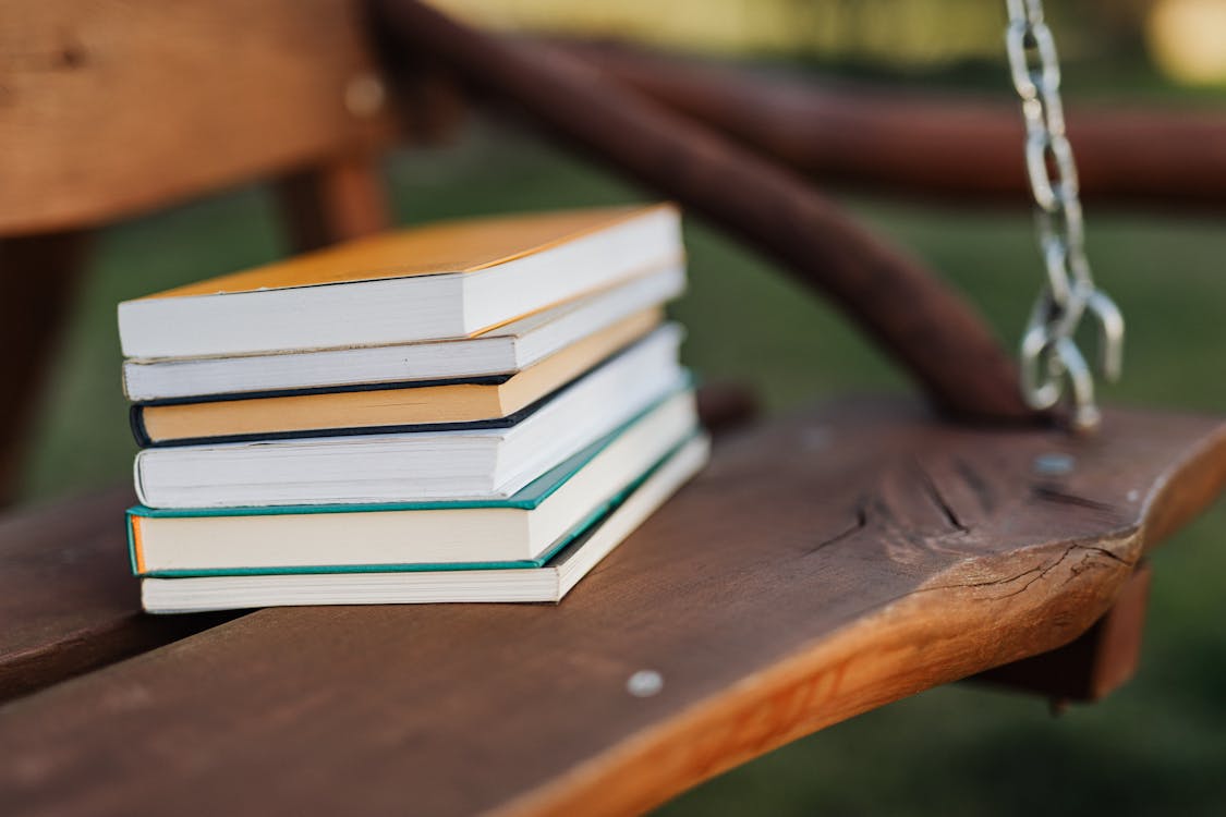 Shallow Focus Photo of Stack of Books Placed on Wooden Swing