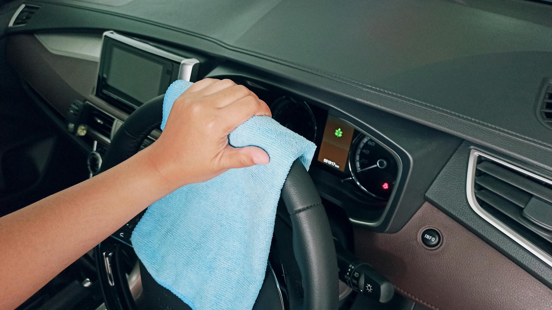 Crop person cleaning car steering wheel with fiber cloth
