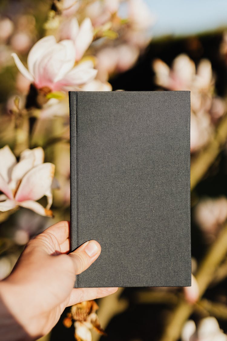 Closed Notebook In Hand Of Unrecognizable Person Against Floral Background