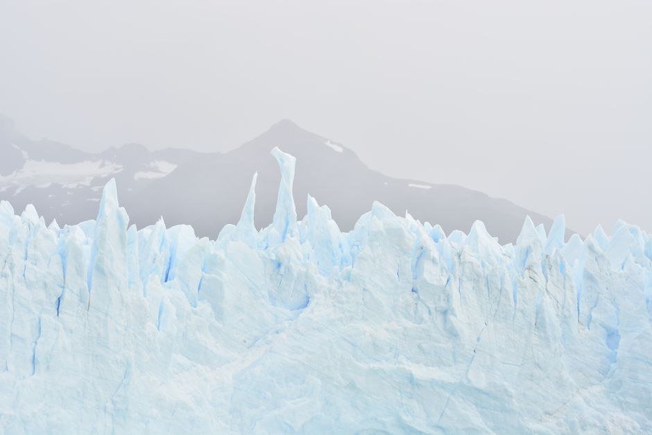 Severe scenery of light blue rough rubble ice in snowy polar highlands against rocky mountains