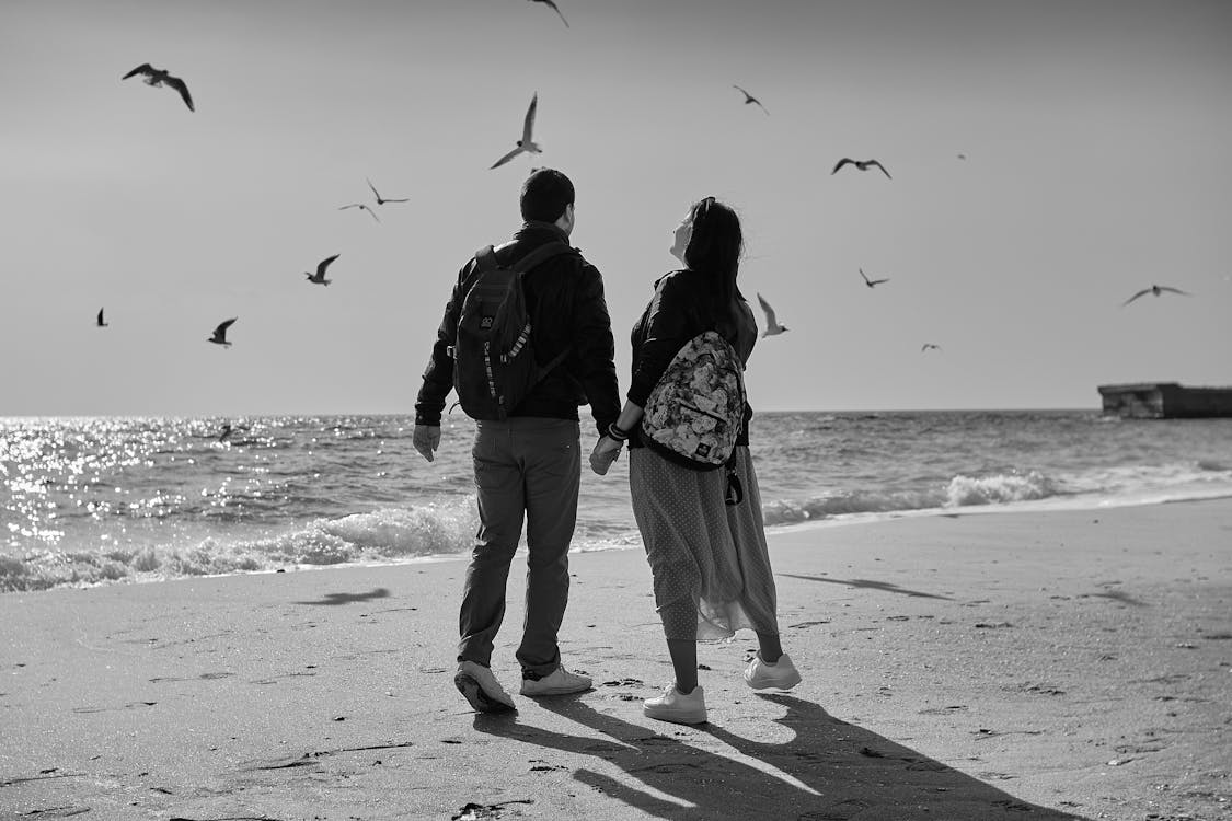 Man and Woman Walking on Beach While Holding Hands