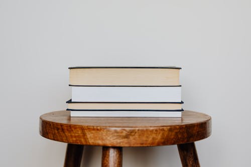 Few books accurately stacked on wooden round original table in front of beige smooth wall