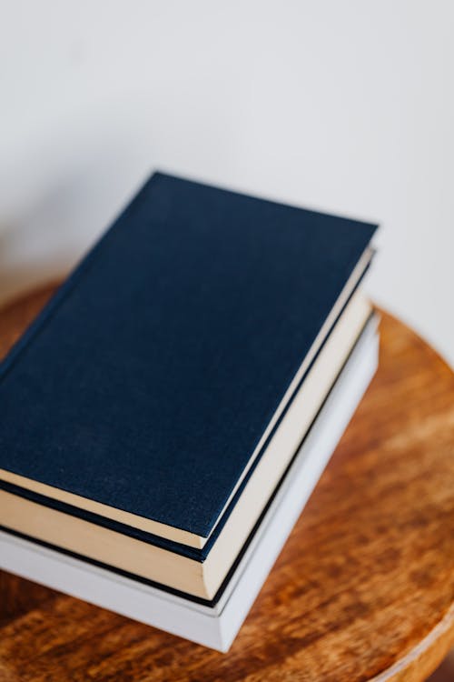 From above of pile of different books stacked on wooden table in front of white wall