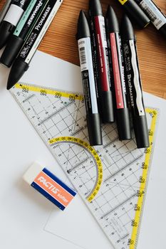 白纸上放着各种记号笔、塑料绘图三角形，以及带有标记的线和数字，它们都位于办公室木桌的橡皮擦附近