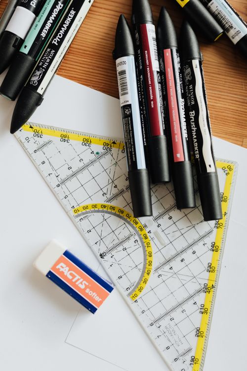 Free Top view of various markers and plastic drawing triangle with marked lines and numbers placed on blank paper near eraser on wooden table in office Stock Photo