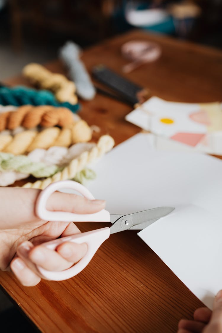 Crop Young Craftswoman Cutting Piece Of Paper On Wooden Table