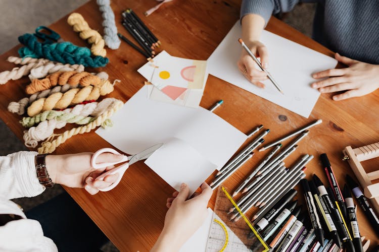 Photo Of Two Persons Drawing And Cutting A White Paper