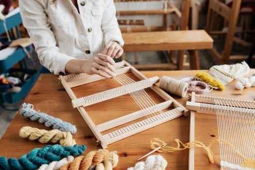 Hands weaving with a loom, surrounded by yarn in a cozy workspace.