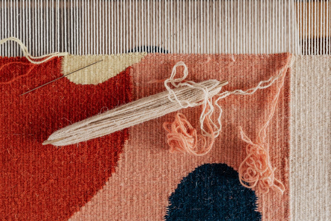 From above of shuttle and needle placed on part of handmade carpet with circle pattern on loom frame during weaving process