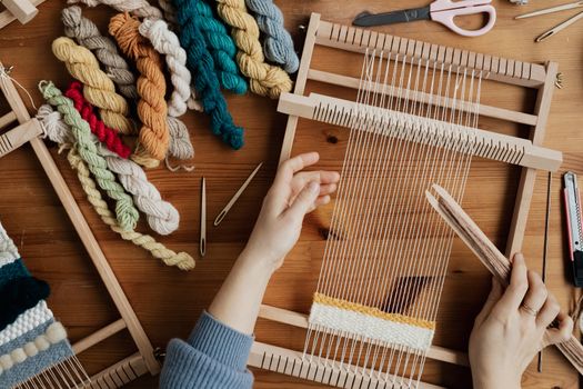 Top view of hands weaving on a wooden loom with colorful yarn, emphasizing craftsmanship and creativity.