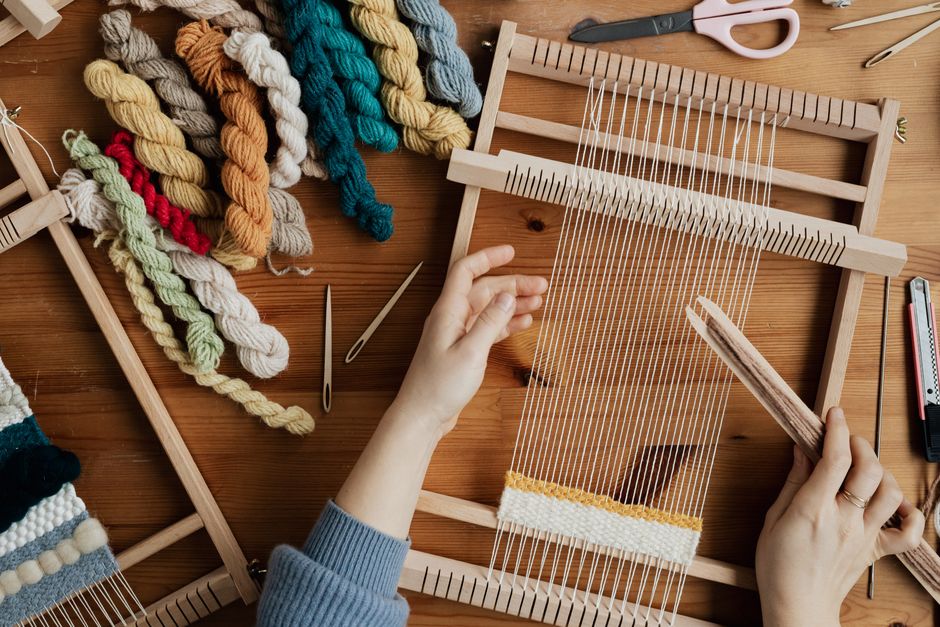 Top view of hands weaving on a wooden loom with colorful yarn, emphasizing craftsmanship and creativity.