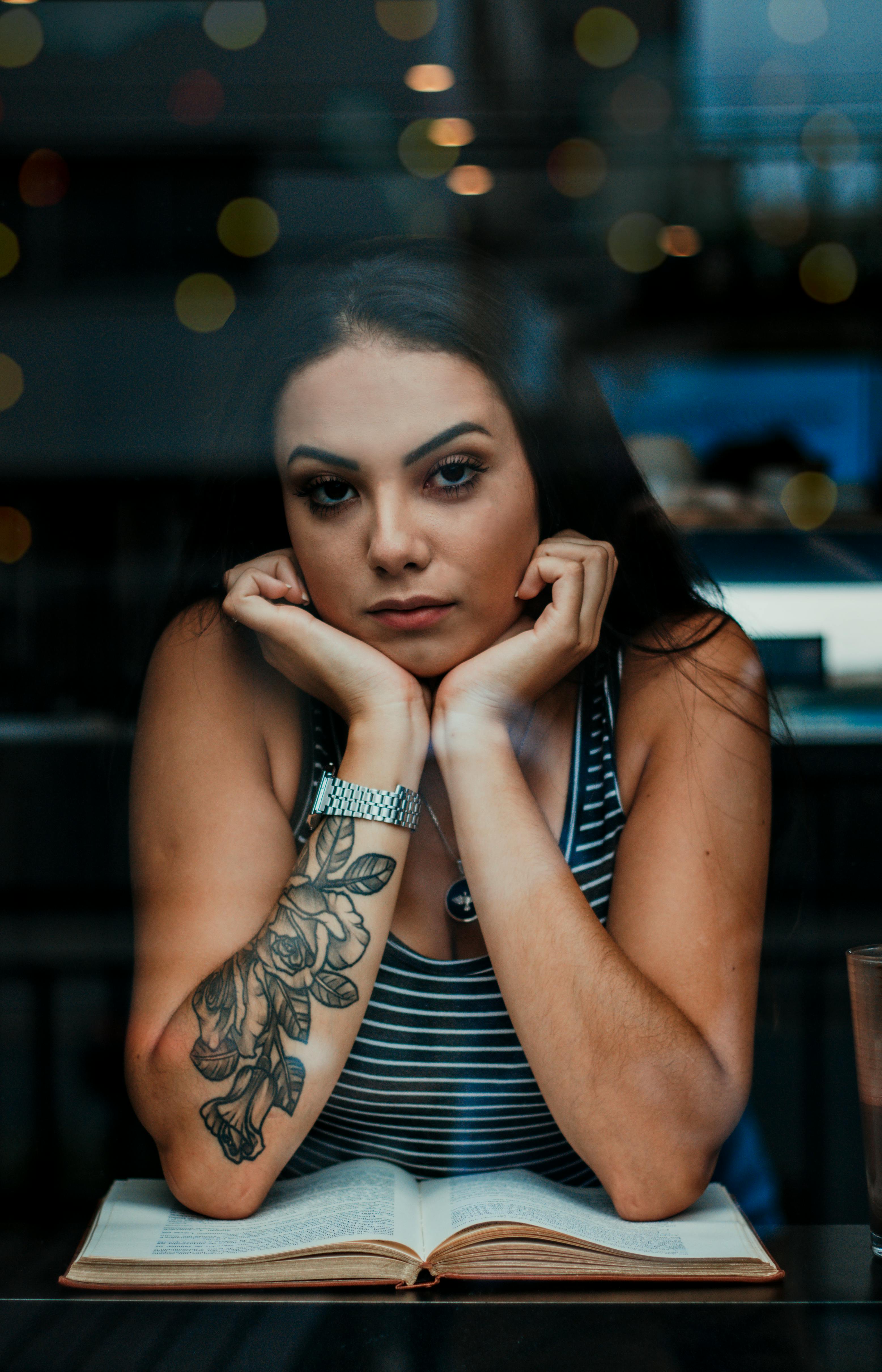 透过窗户拍摄的一位坐在室内沉思、纹身的女人的特写镜头