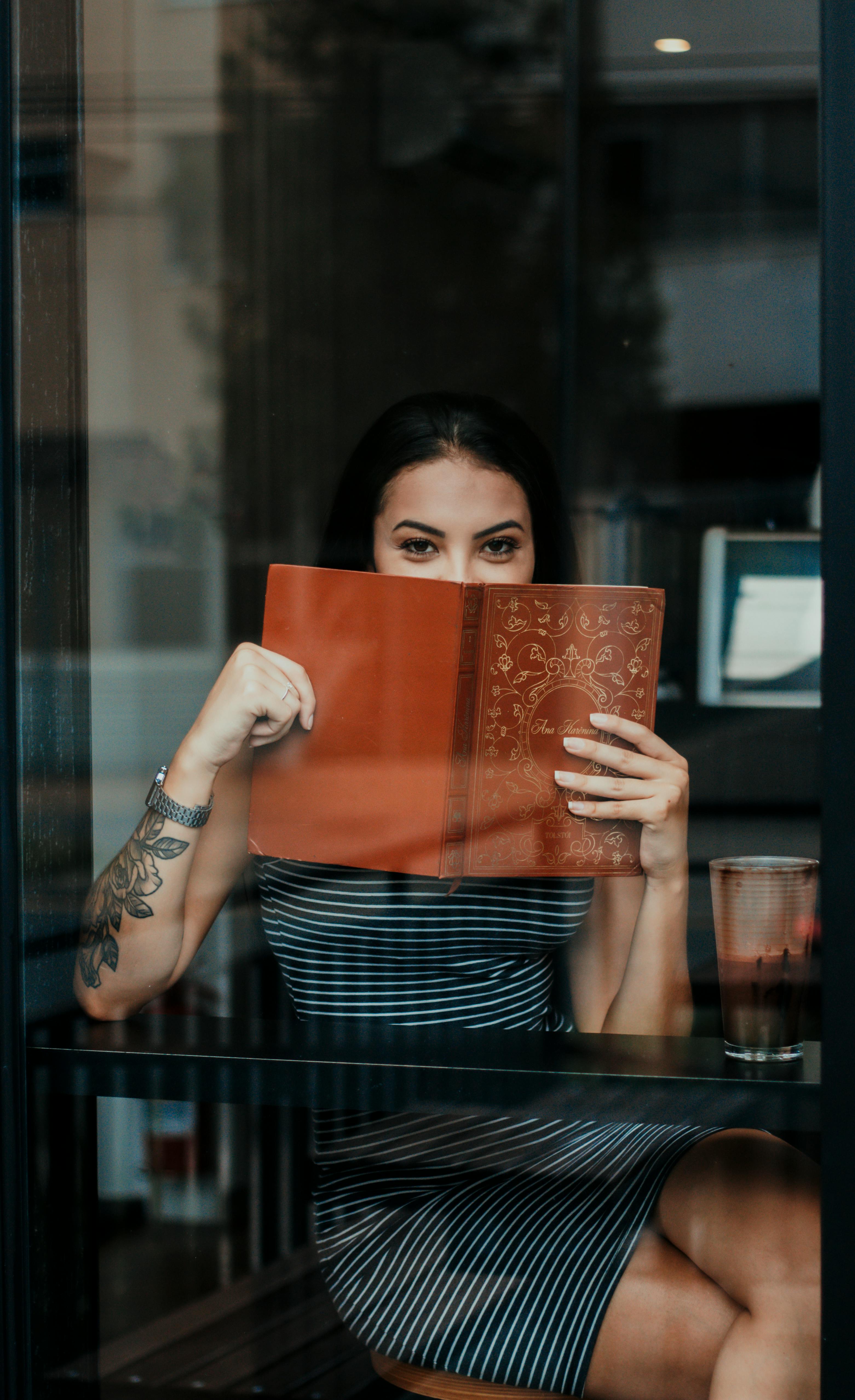 cheerful woman covering mouth with menu while relaxing in cafeteria