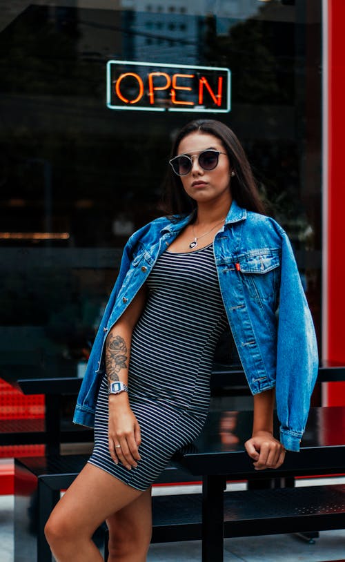 Woman in Black and White Striped Dress Wearing Blue Denim Jacket and Black Sunglasses