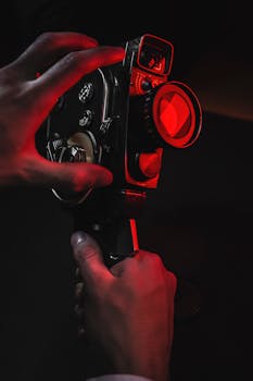A close-up shot of hands holding an analog vintage camera under dramatic red lighting.